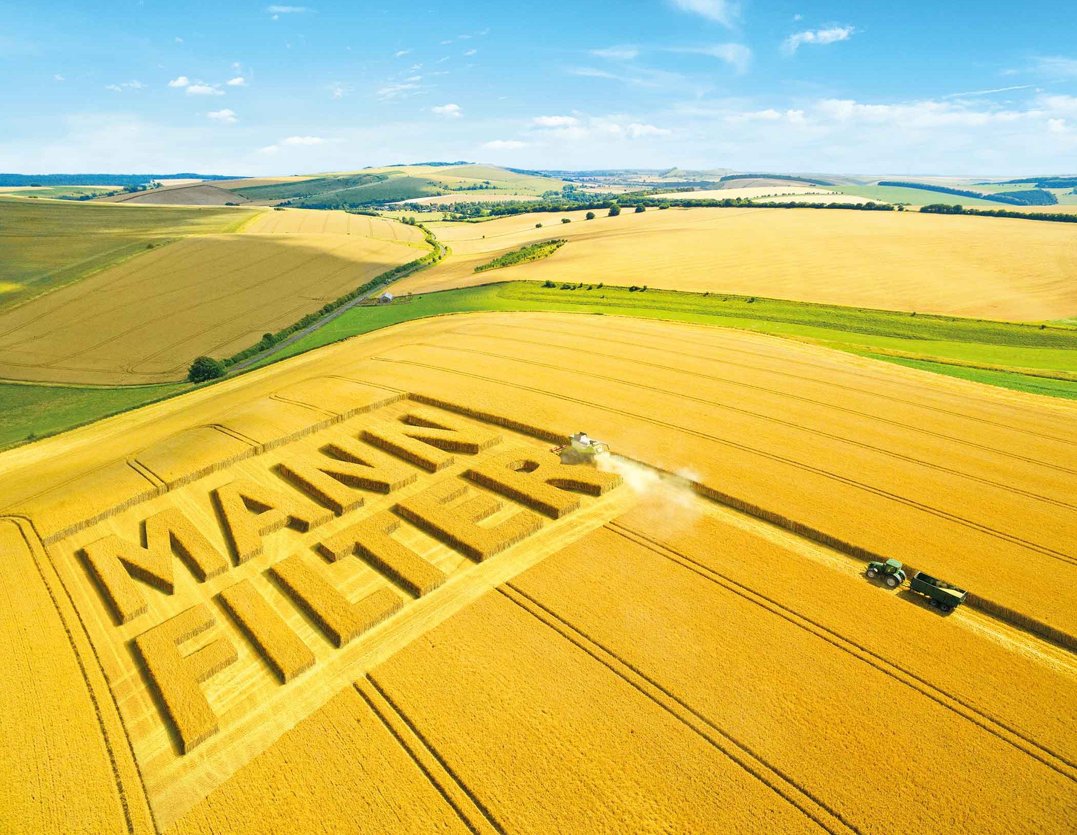 Aerial view of a golden field with MANN-FILTER logo cut into crops and tractors harvesting