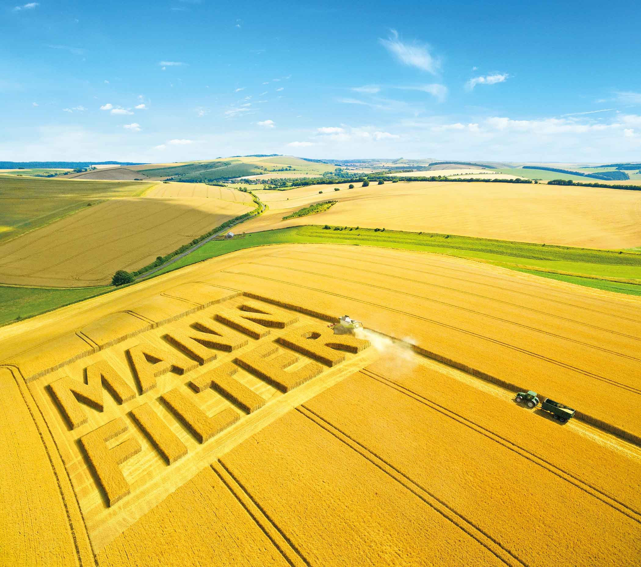 Luftaufnahme eines goldenen Feldes mit eingeschnittenem MANN-FILTER Logo und Traktoren bei der Ernte