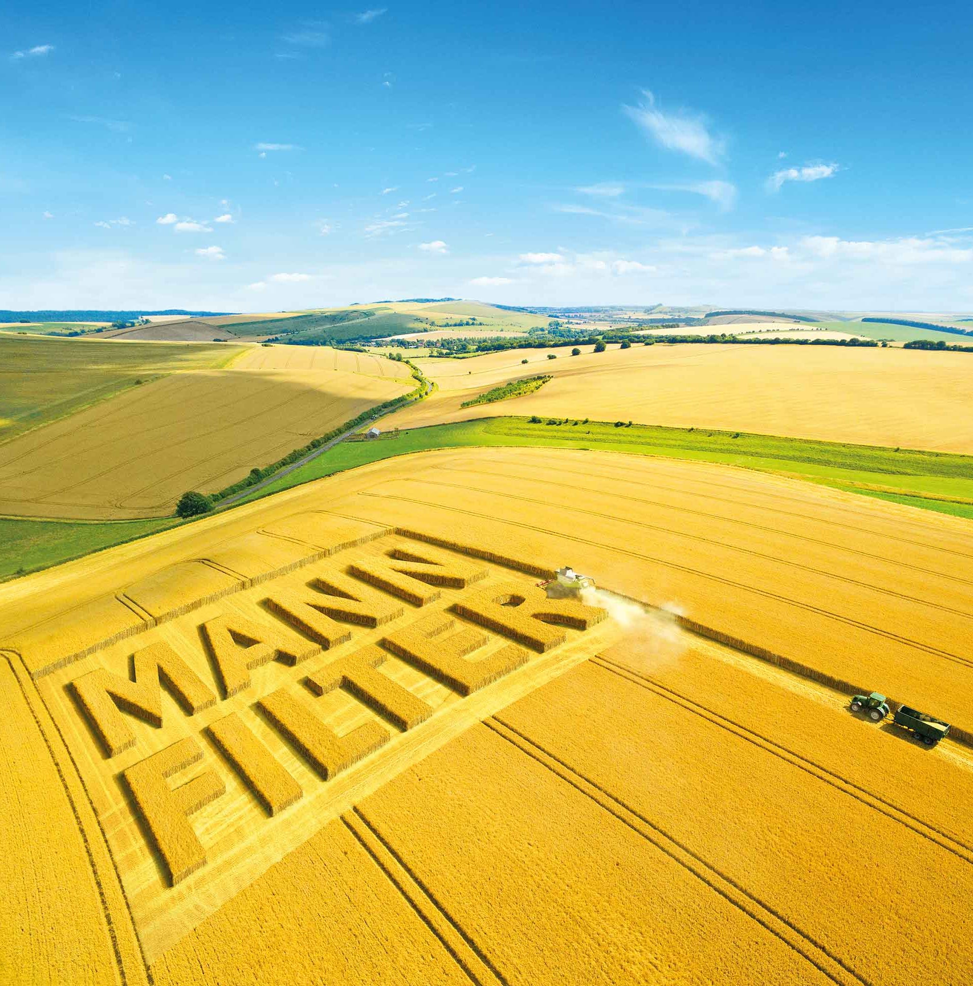 Aerial view of a golden field with MANN-FILTER logo cut into crops and tractors harvesting