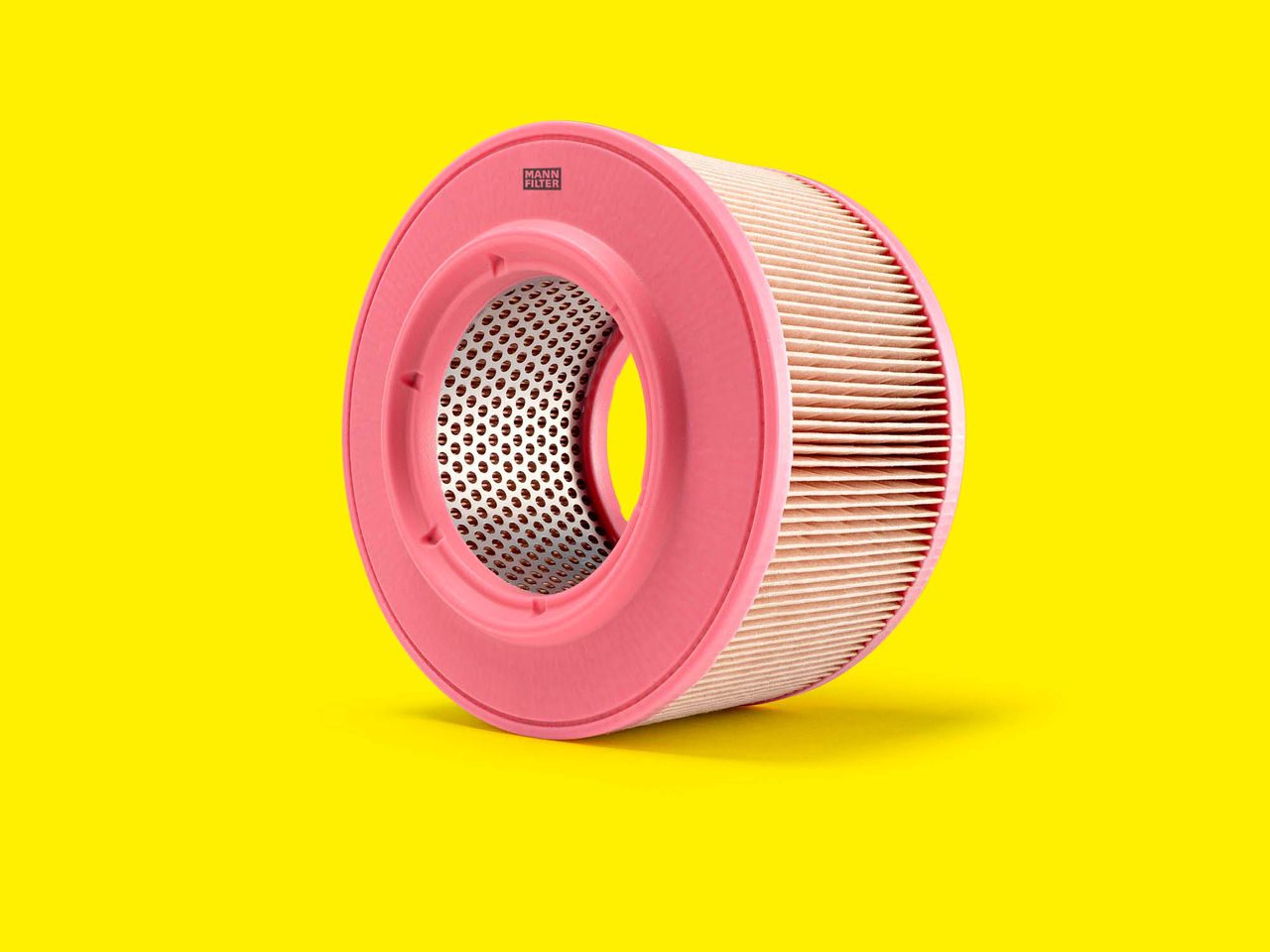 A round MANN-FILTER air filter with a pink and white design displayed on a yellow background