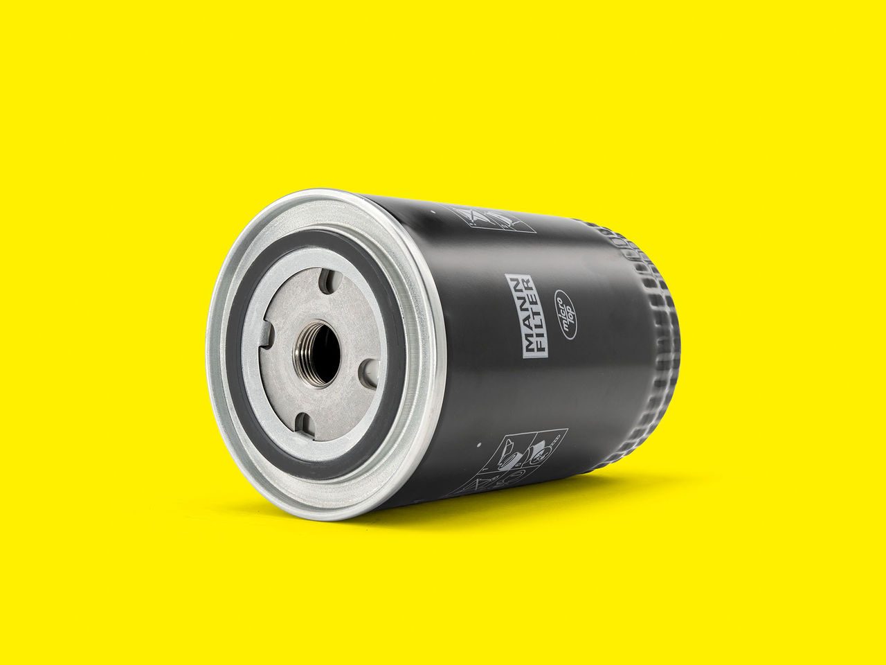A black and silver MANN-FILTER coolant filter displayed against a bright yellow background