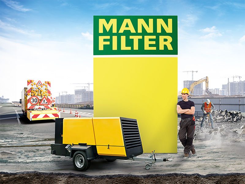 A portable compressor with a worker on a construction site and a large MANN-FILTER logo displayed