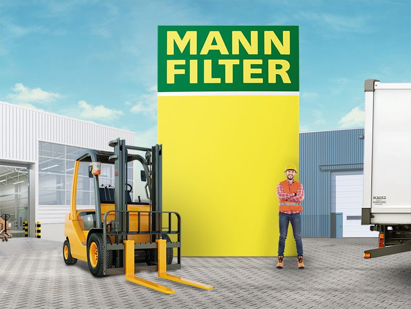 A forklift and a worker standing near a truck with a large MANN-FILTER logo in the background