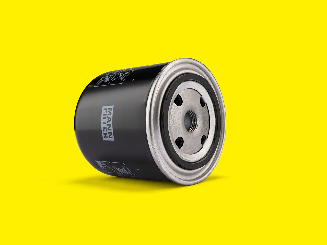 Black MANN-FILTER coolant filter with a metal base, displayed on a bright yellow background