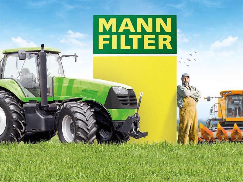 Green agricultural tractor and farmer near MANN-FILTER branding with a harvester in the background