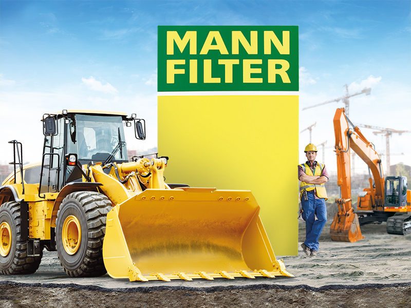 Yellow loader, worker, and excavator near MANN-FILTER branding at a construction site