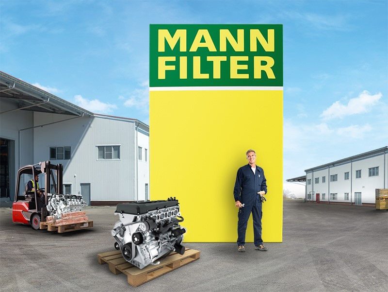 Industrial engine, mechanic by MANN-FILTER box, forklift and warehouse in background with blue sky