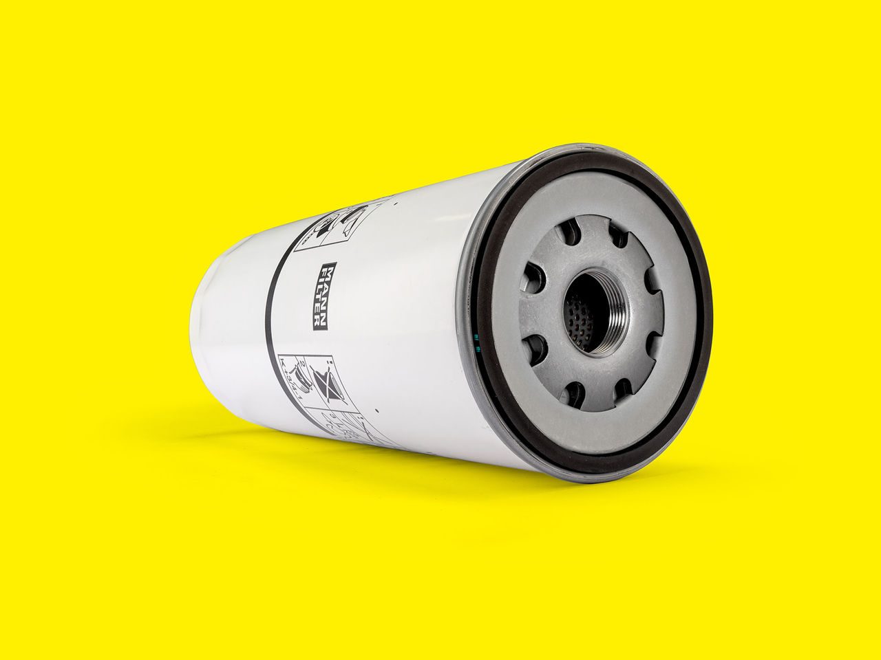 White MANN-FILTER oil filter with metal base and threaded center on a yellow background