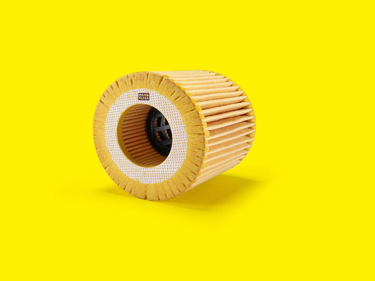 Cylindrical MANN-FILTER oil filter element with pleated design on a bright yellow background