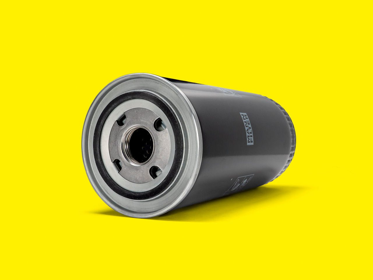A black and silver MANN-FILTER oil filter for compressors and vacuum pumps on a yellow background