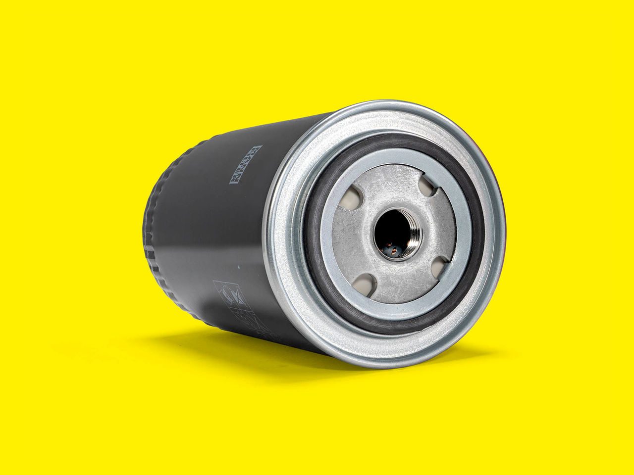 A black and silver MANN-FILTER oil filter displayed against a bright yellow background