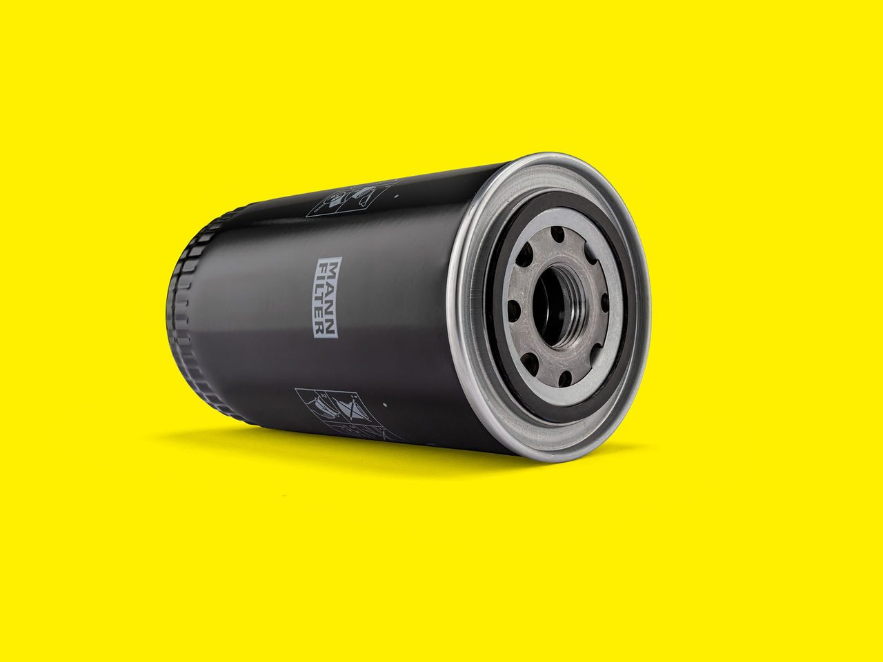 Black MANN-FILTER transmission oil filter with a metal threaded base on a yellow background