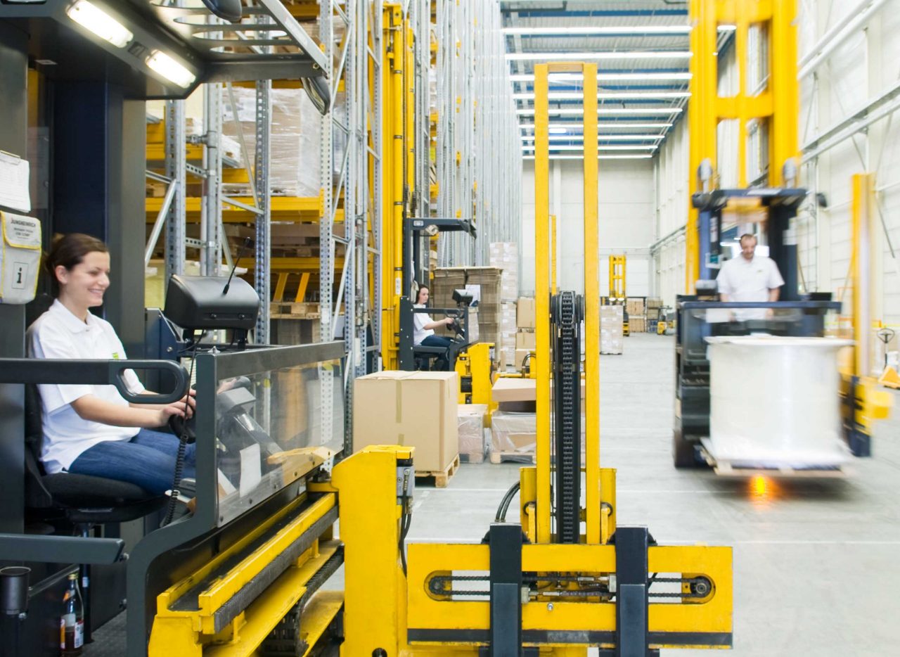 A forklift operating in a warehouse with a worker in the foreground and MANN-FILTER branding