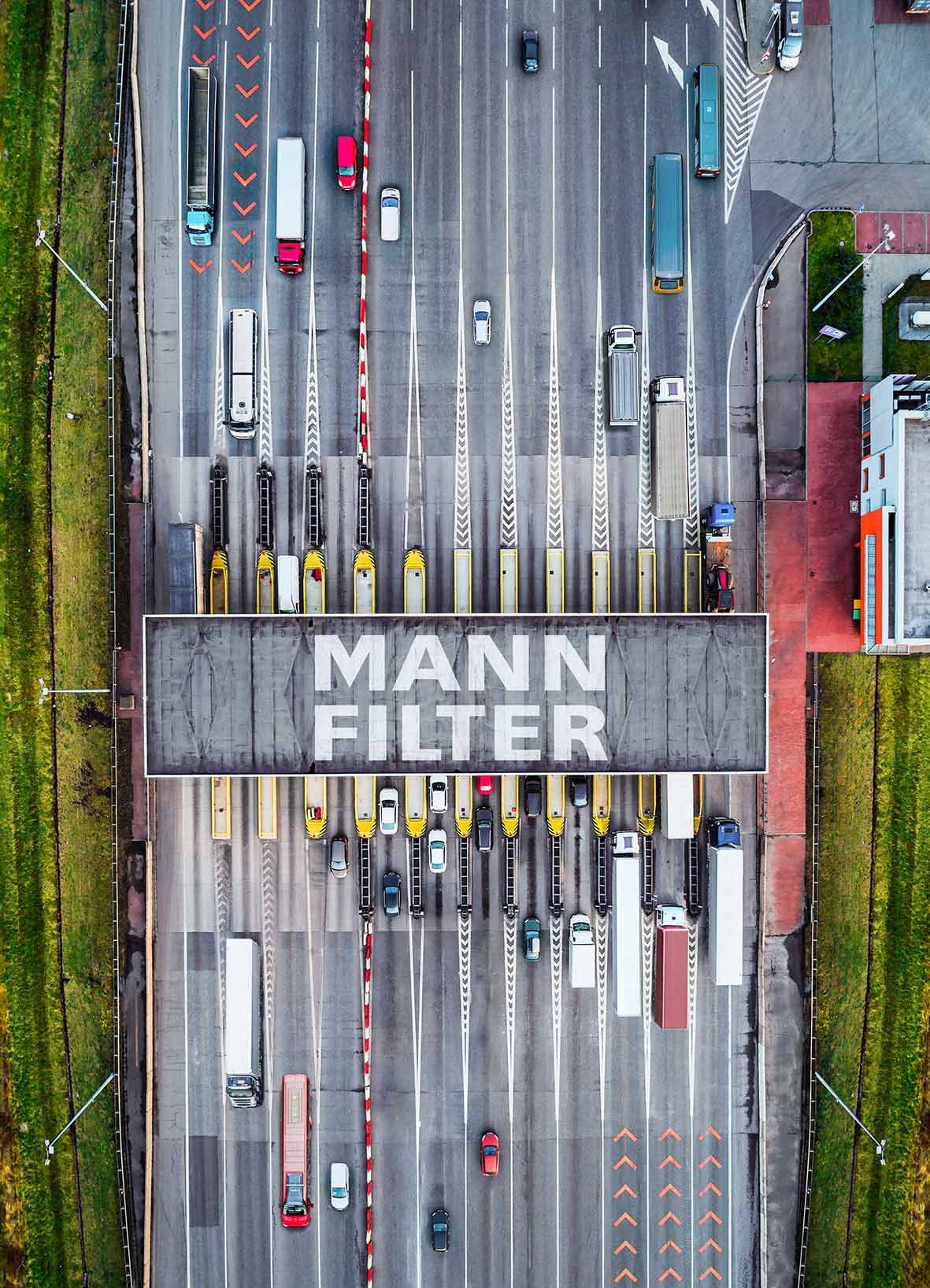 Vista aérea de estación de peaje con la marca MANN-FILTER, rodeada de camiones y autobuses
